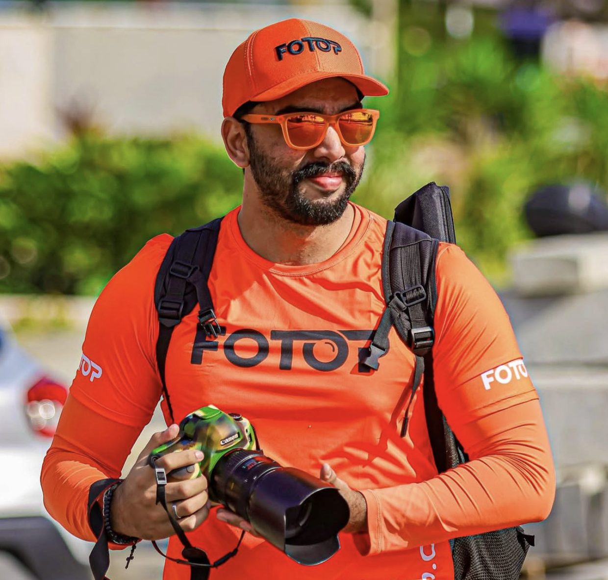 Fotop photographer in an orange cap and shirt holding a camera with a telephoto lens. Photographers should know how to watermark photos.