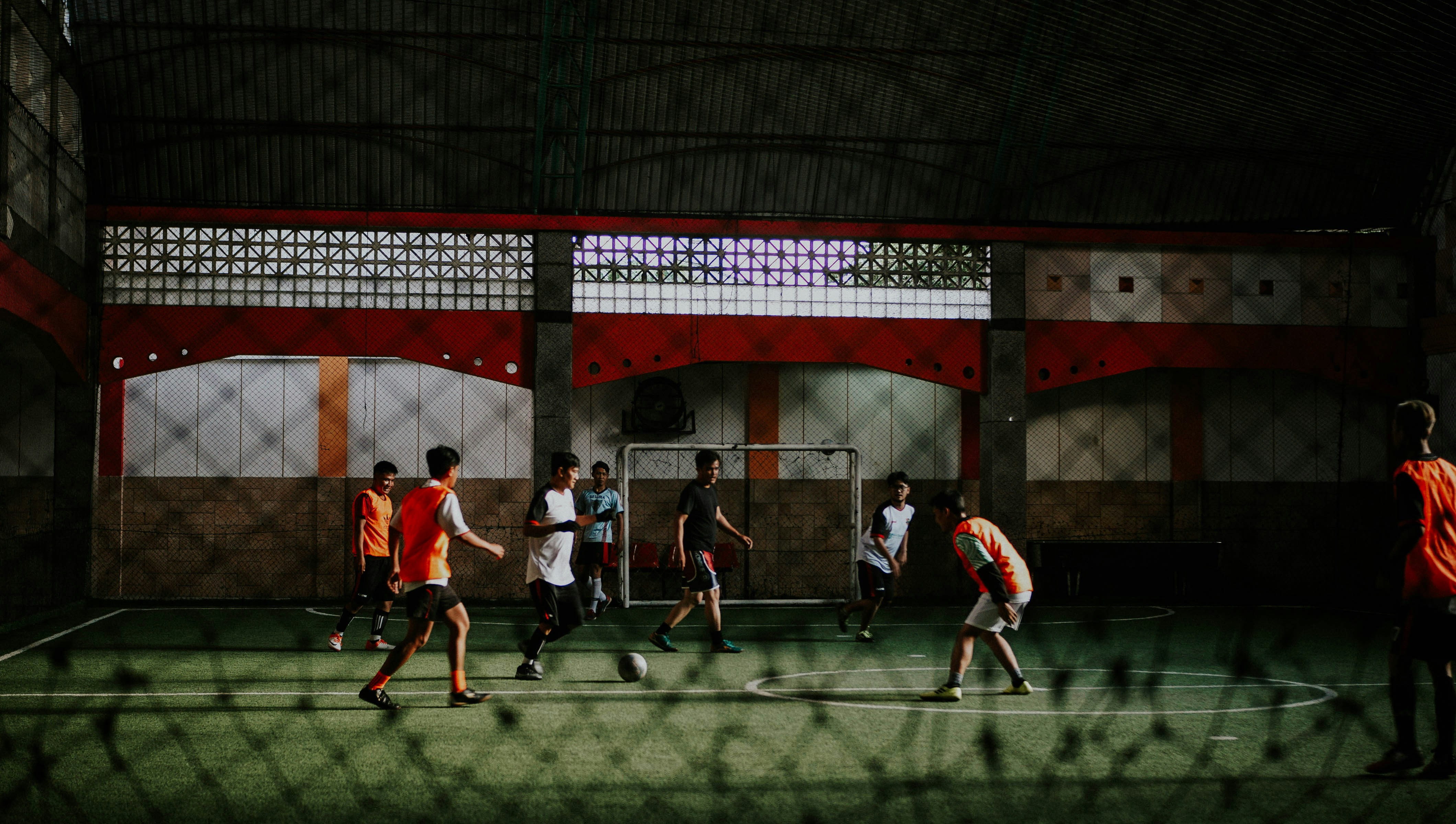 Jogadores disputam partida em quadra coberta, com bola em jogo, em uma cena de fotos de futsal em ação.